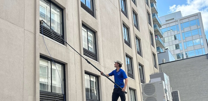 Vincent, technicien VitresMV, utilisant une perche télescopique pour laver les vitres d'un immeuble commercial dans l'Ouest-de-l'Île