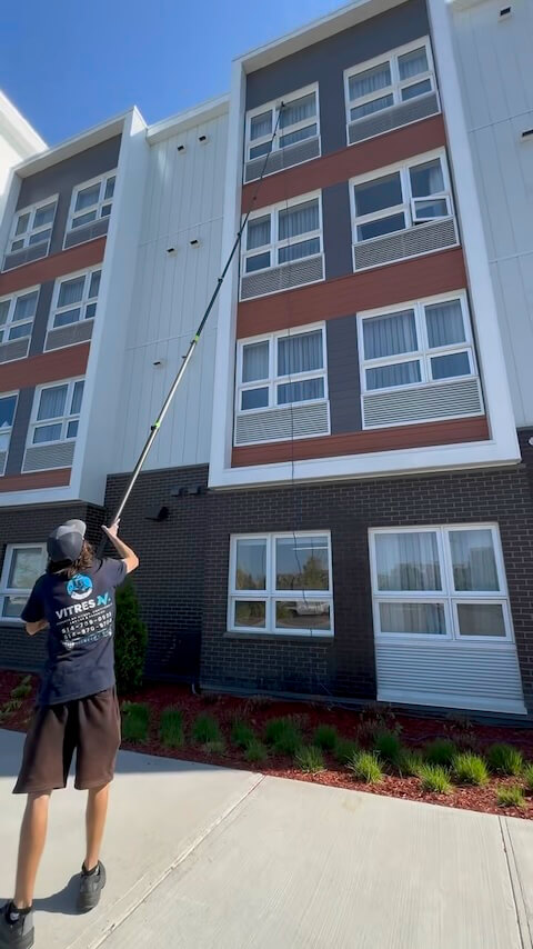 Vincent, technicien VitresMV, utilisant une perche télescopique pour laver les vitres d'un immeuble dans l'Ouest-de-l'Île